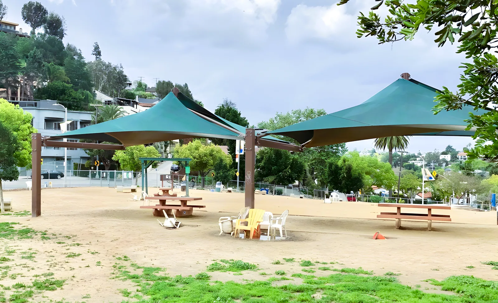 Fenced dirt park with teal shade sails and picnic tables