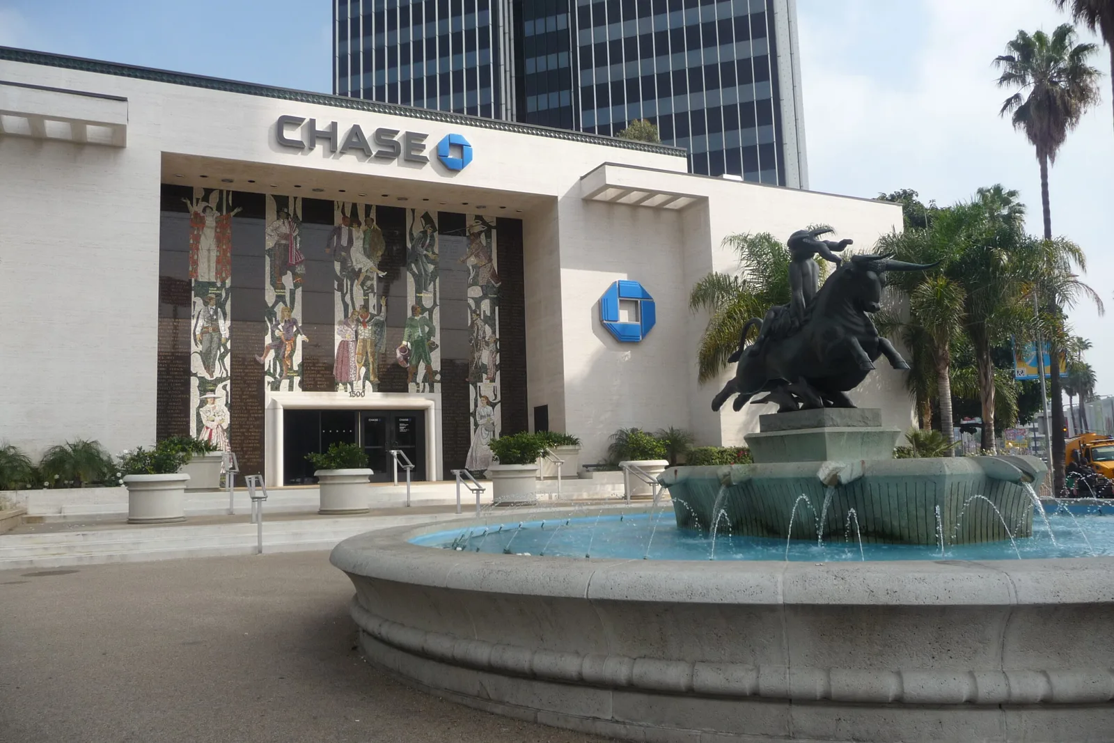 White bank branch building behind a stone fountain and sculpture