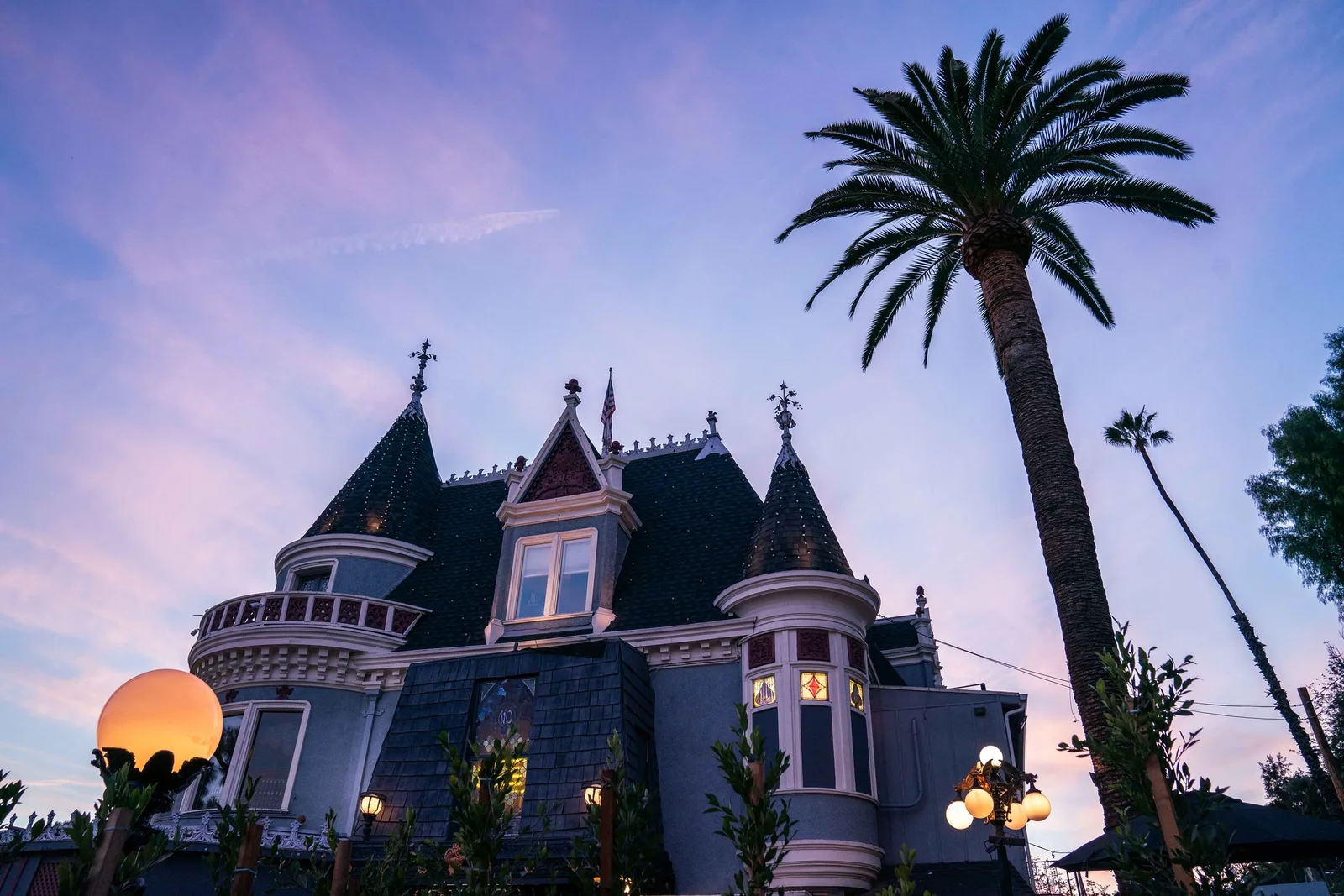 Turreted Victorian mansion at dusk framed by tall palm trees