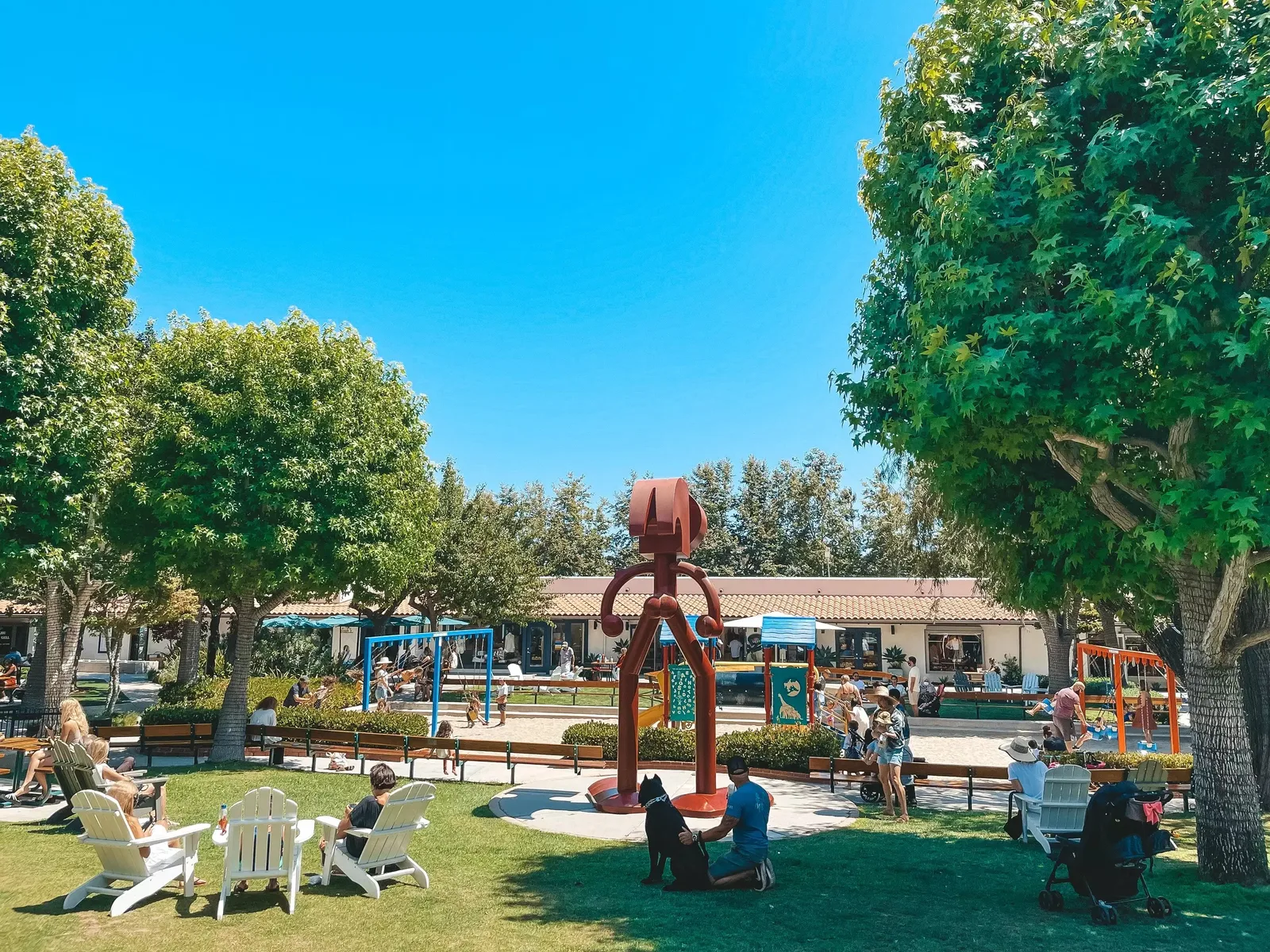 Lawn with seated visitors, a red sculpture and shops beyond