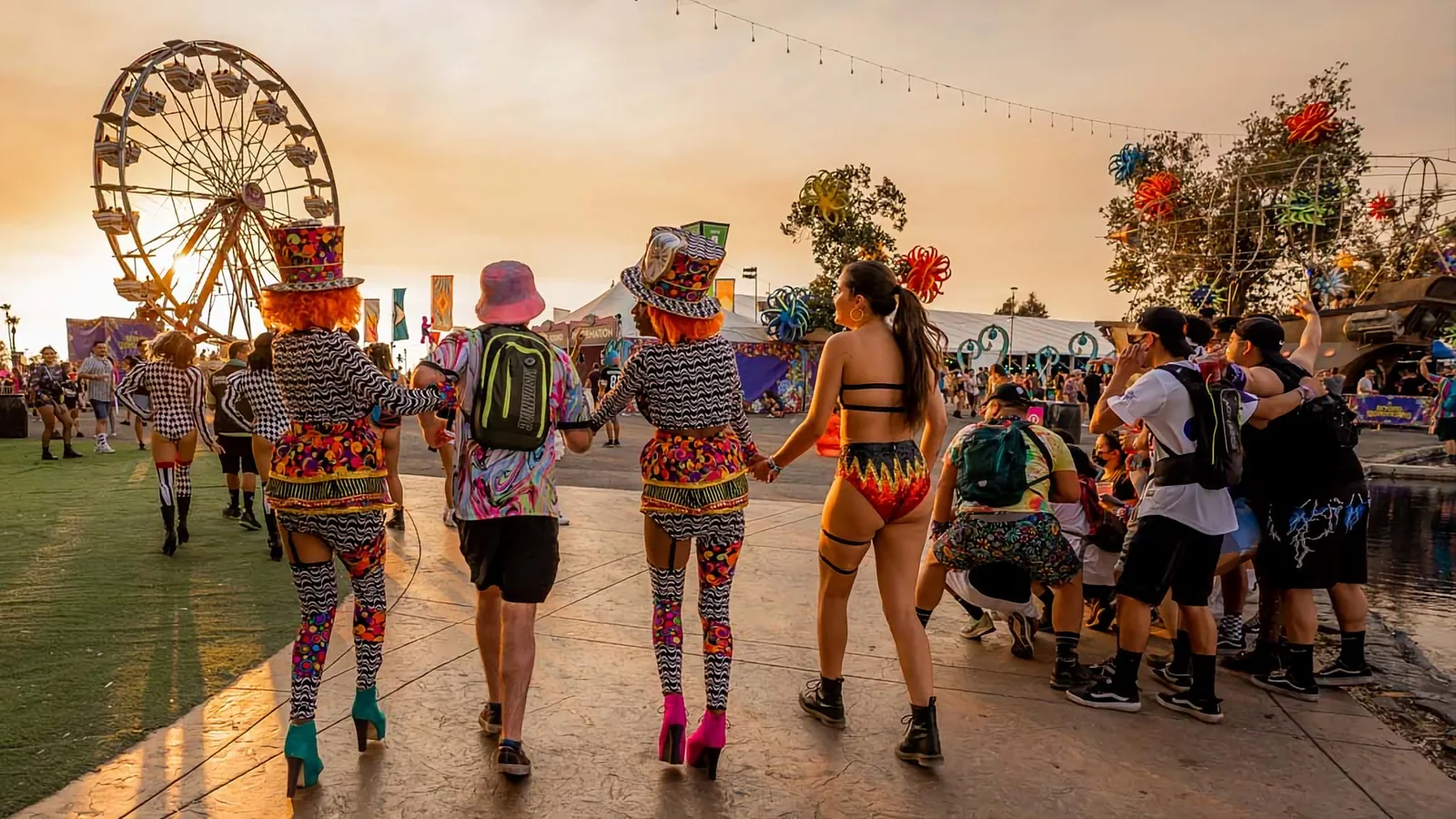 Festival-goers entering a music festival with a ferris wheel and colorful tents in the background.