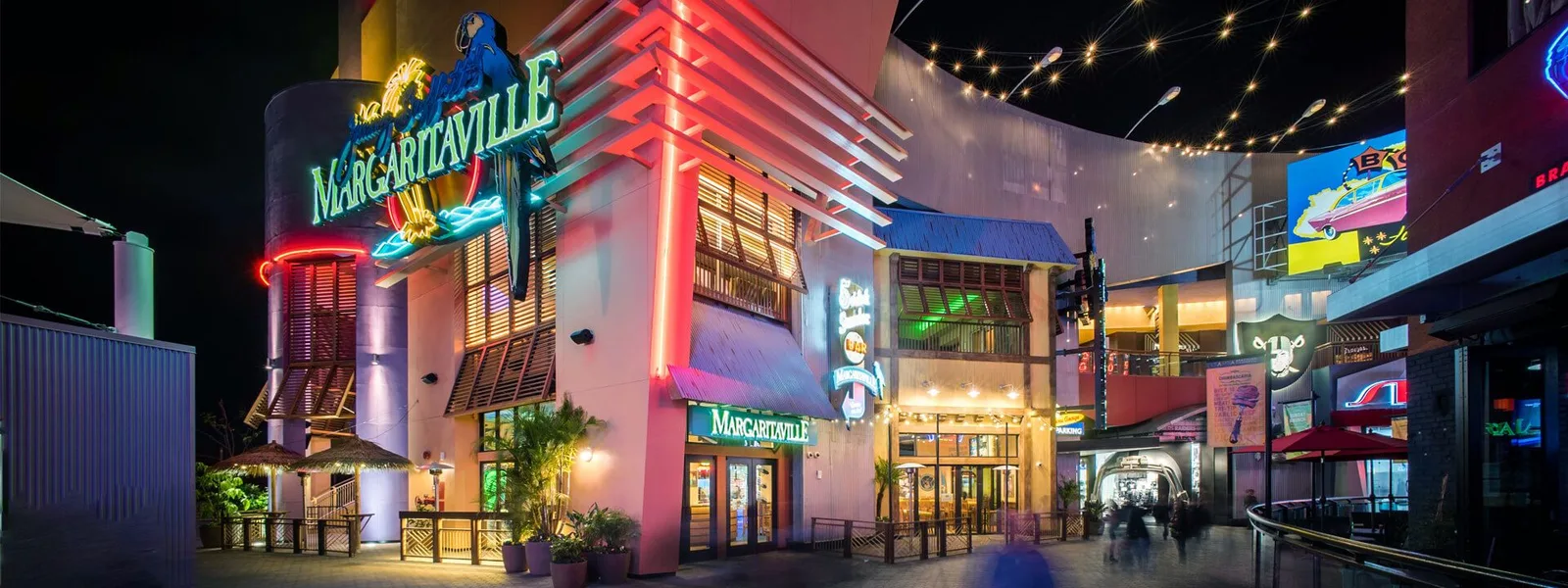 Neon-lit shopping walkway at dusk with palm trees
