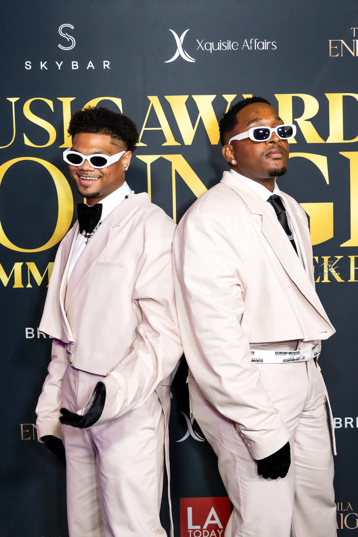 Two guests in pale pink suits and sunglasses pose back to back