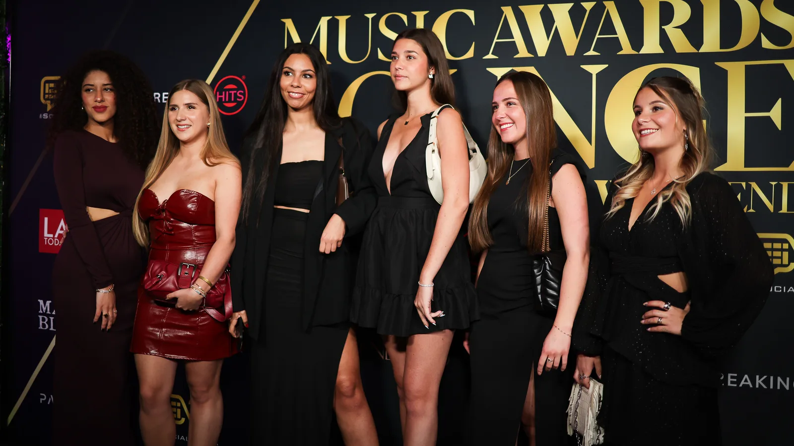 Six guests in dark cocktail dresses line up on the red carpet