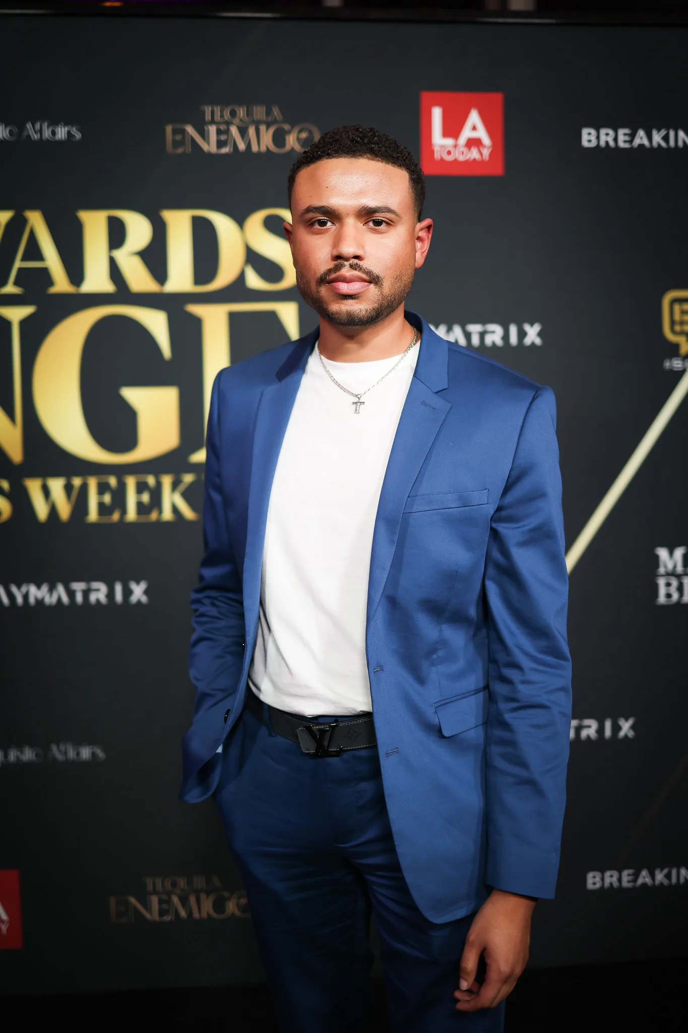 A guest in a blue blazer and white tee poses at the step-and-repeat