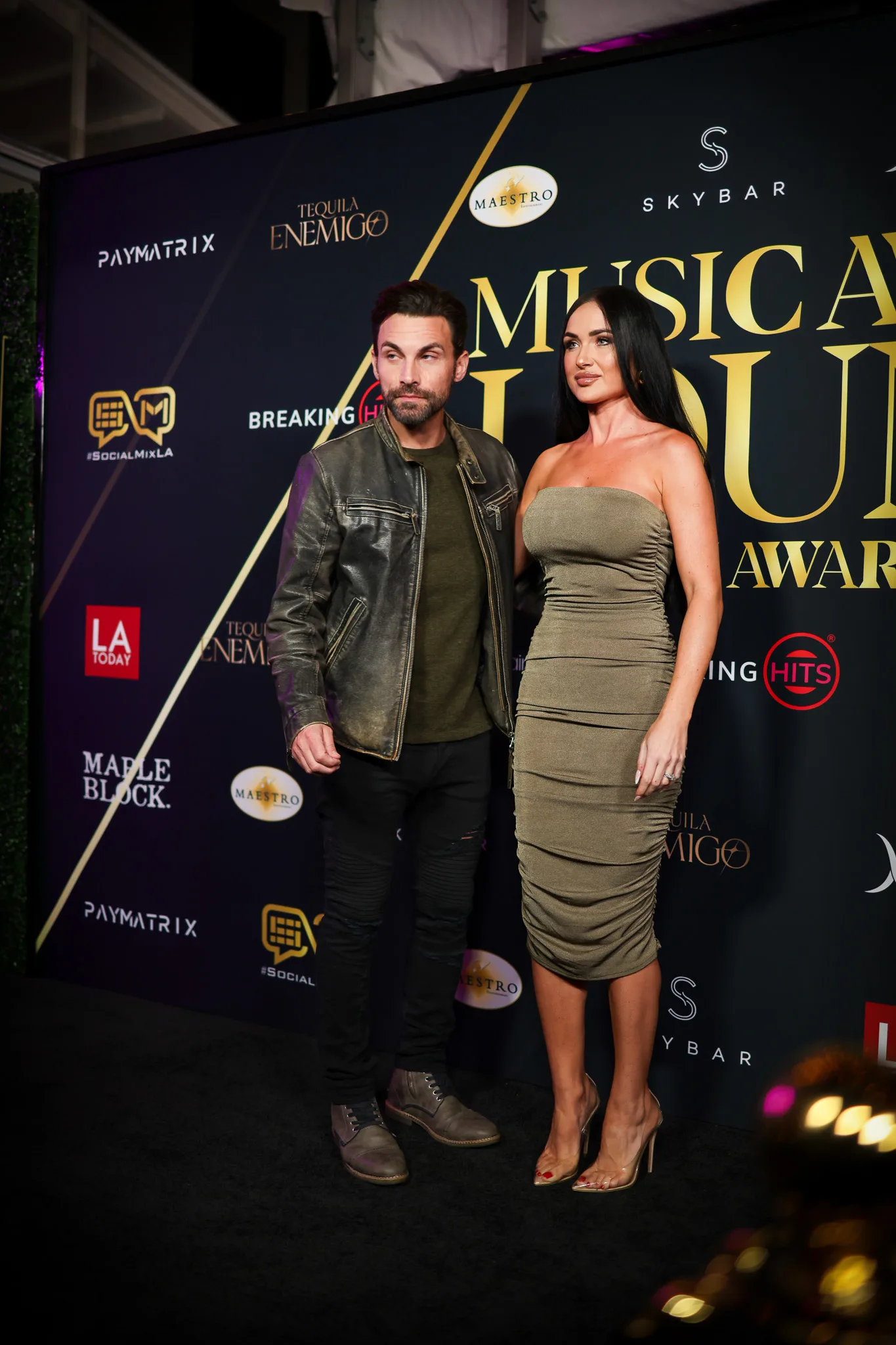 Two guests pose together, one in a leather jacket, one in olive