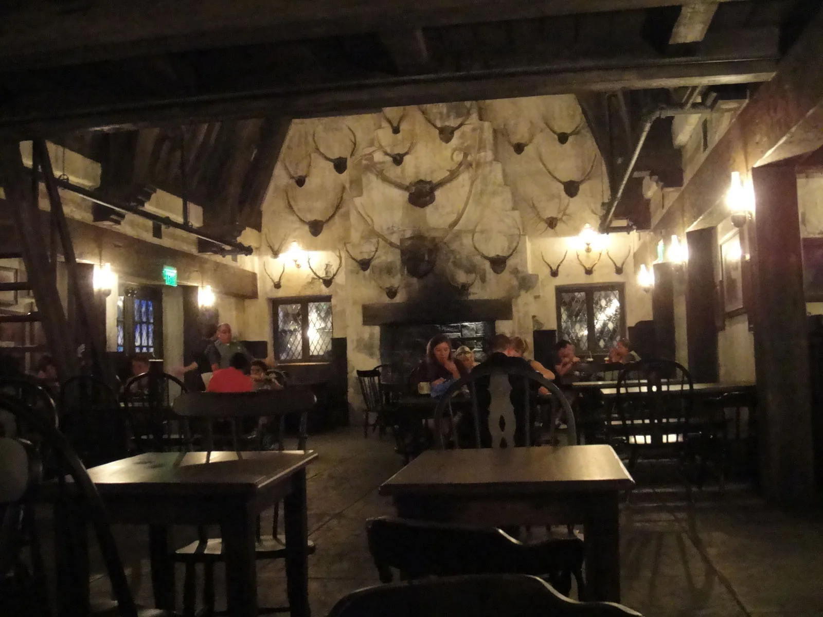 Dim timber beamed tavern interior with long wooden tables and benches