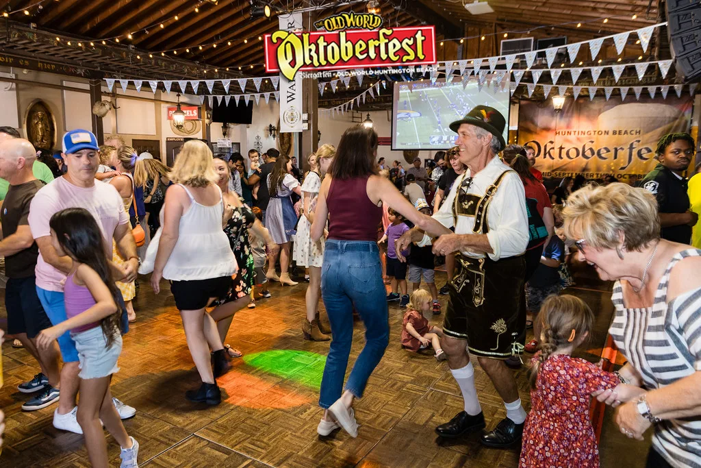 Crowd dancing in a festival hall with bunting and a man in lederhosen