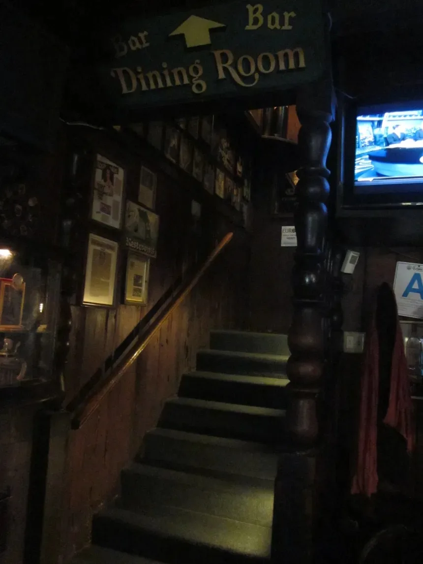 Dark wood tavern interior with framed pictures and a stairway