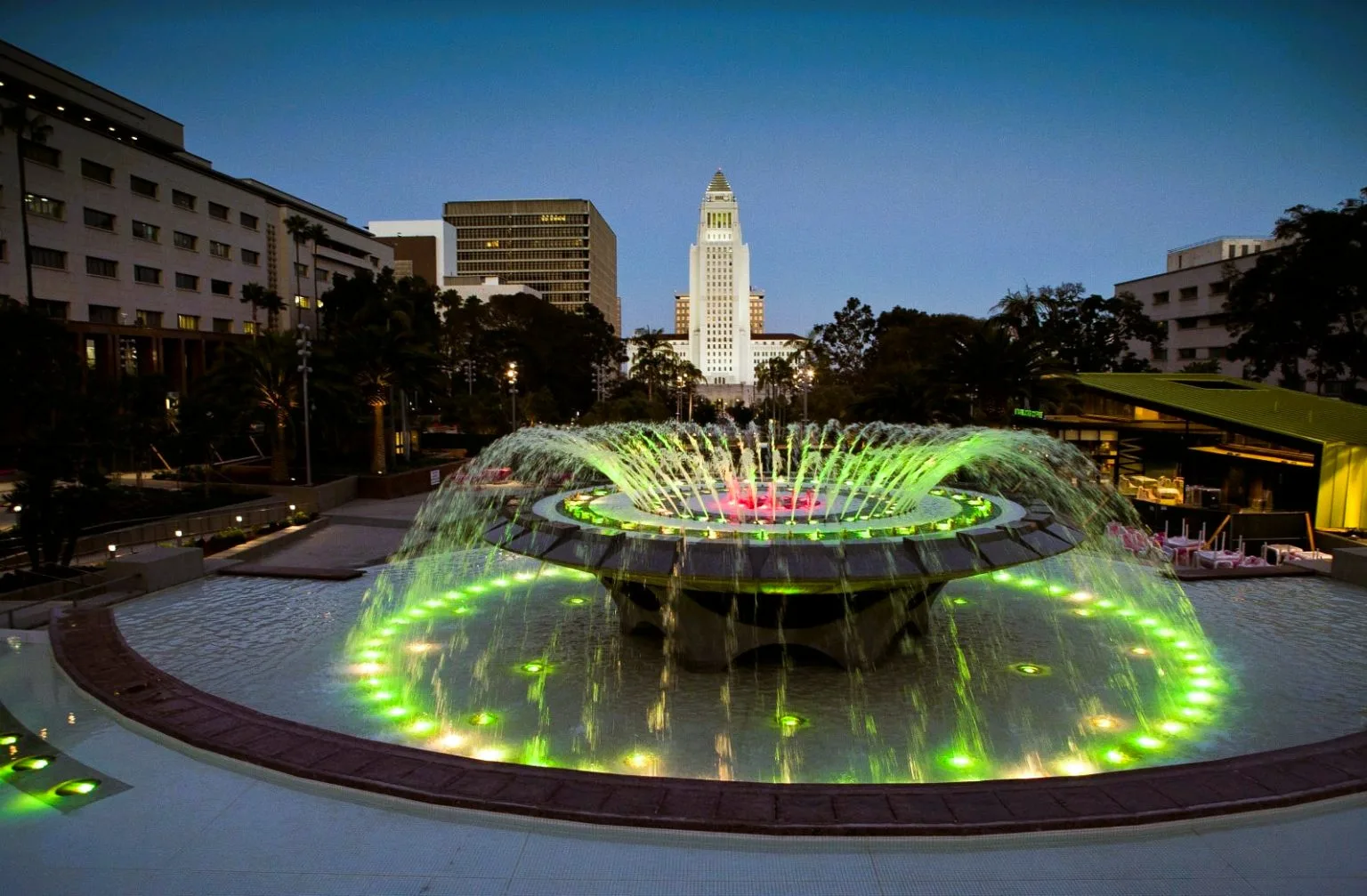 The Arthur J. Will Memorial Fountain lit green at Gloria Molina Grand Park, with Los Angeles City Hall behind it