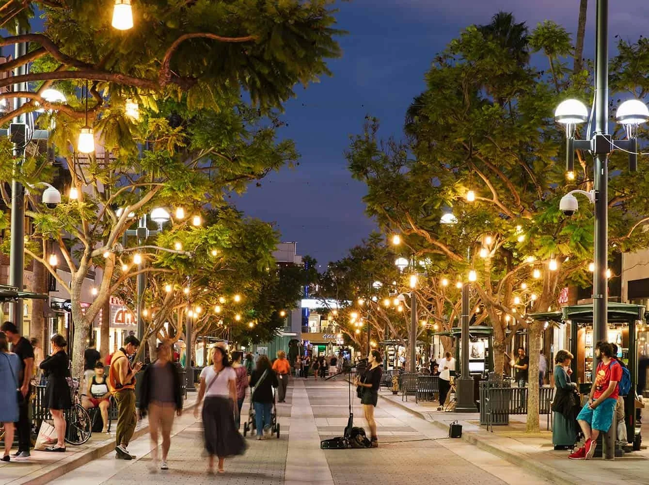 Evening promenade strung with lights in trees as people walk past
